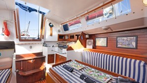 Cabina de barco con cama, una mesita, un mapa y ventana con vista al mar.
