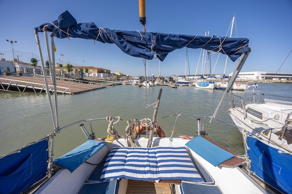 A boat with a blue canopy, a wooden deck, and a view of a marina with other boats.