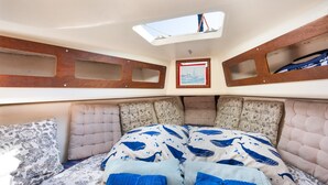 Interior de barco con cama, almohadas y tragaluz.
