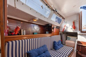 Ein Bootsinnenraum mit einer gestreiften Couch, einem kleinen Tisch und einem Fenster mit Blick zum Himmel.