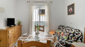 A room with a dining table set, a sofa, a television on a wooden cabinet, and a window with curtains.