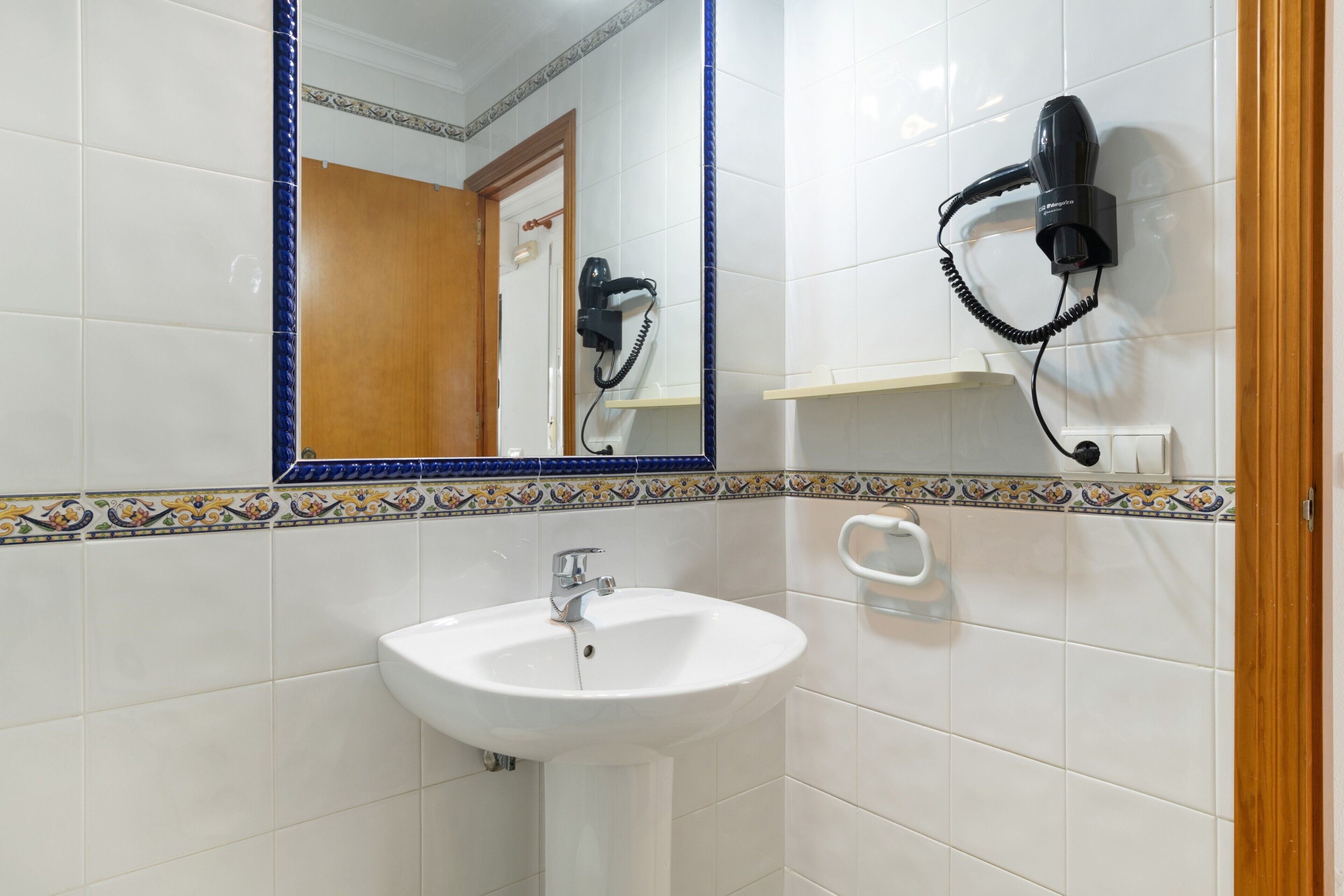 Une salle de bain avec un lavabo blanc, un miroir doté d’un cadre bleu et un sèche-cheveux fixé au mur.