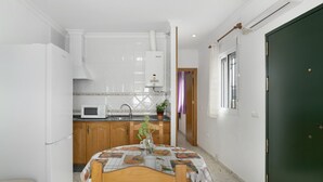A compact kitchen with white cabinets, a microwave, and a dining table with a fruit-patterned tablecloth.