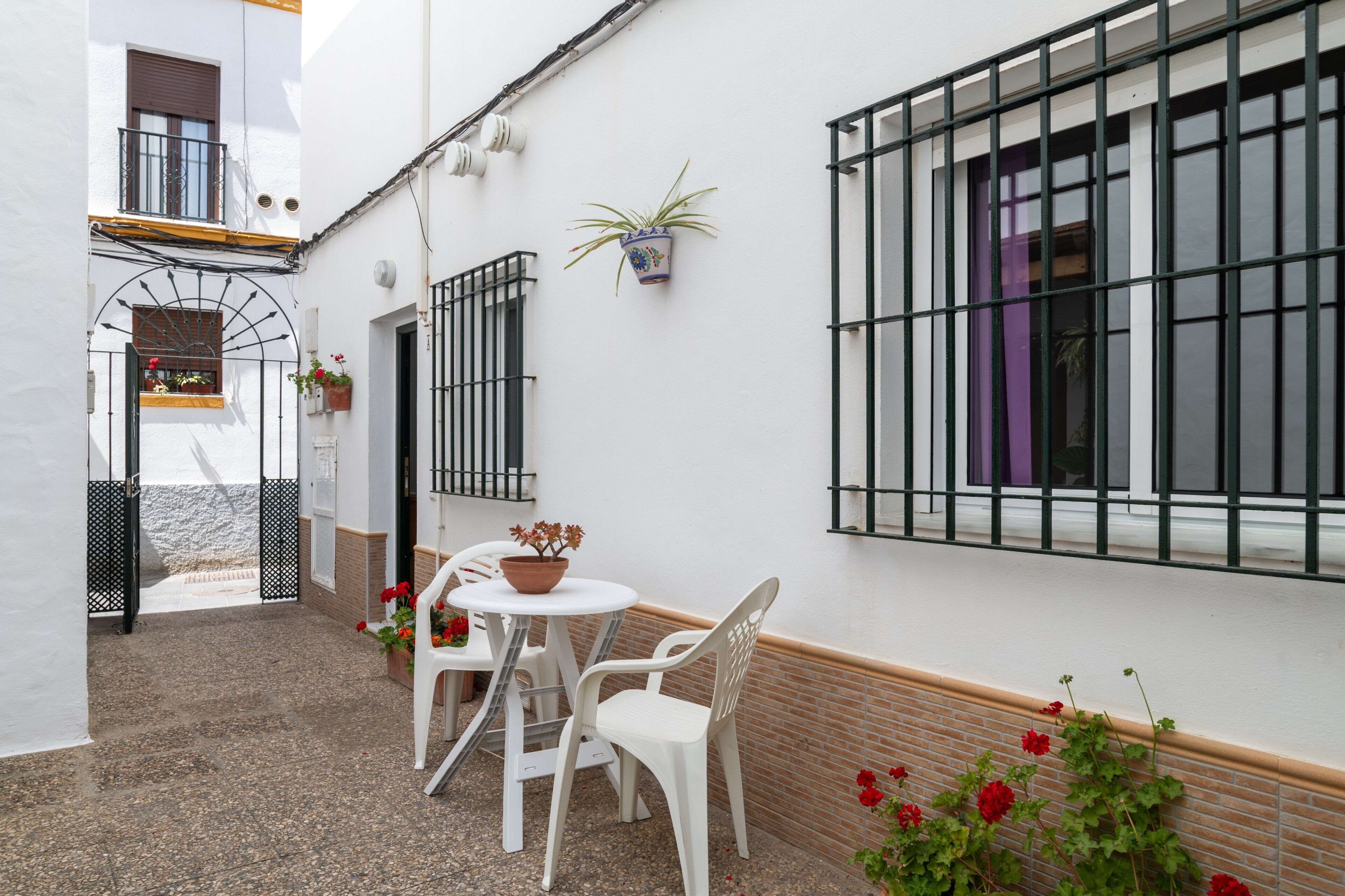 A courtyard with a table and chairs, potted plants, and a window with bars.