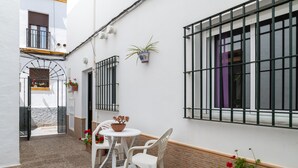 A courtyard with a table and chairs, potted plants, and a window with bars.