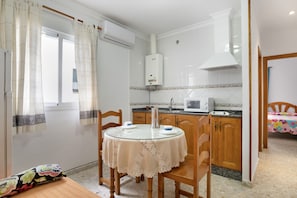 Une cuisine compacte avec une table ronde, des chaises en bois, un four à micro-ondes et un chauffe-eau.