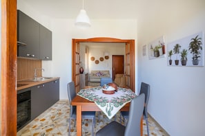 Een compacte keuken met moderne apparatuur, een eetgedeelte met een tafel voor twee en een woonruimte met een bank en decoratieve muurkunst.