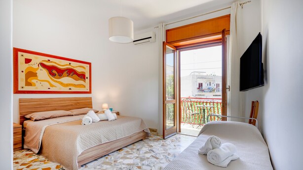 A hotel room with a bed, a smaller bed, a TV, a painting, and a balcony with a view. - Casa Merlino - Triple Room with Balcony (Santo Spirito)