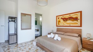 A bedroom with a bed, a wooden headboard, a nightstand with a lamp, a mirror, and a painting on the wall. - Casa Merlino - Triple Room with Balcony (Santo Spirito)