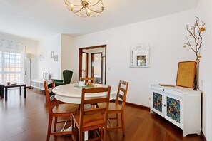 Zona pranzo con tavolo rotondo, sedie in legno, un armadietto bianco con pannelli decorativi e un lampadario.