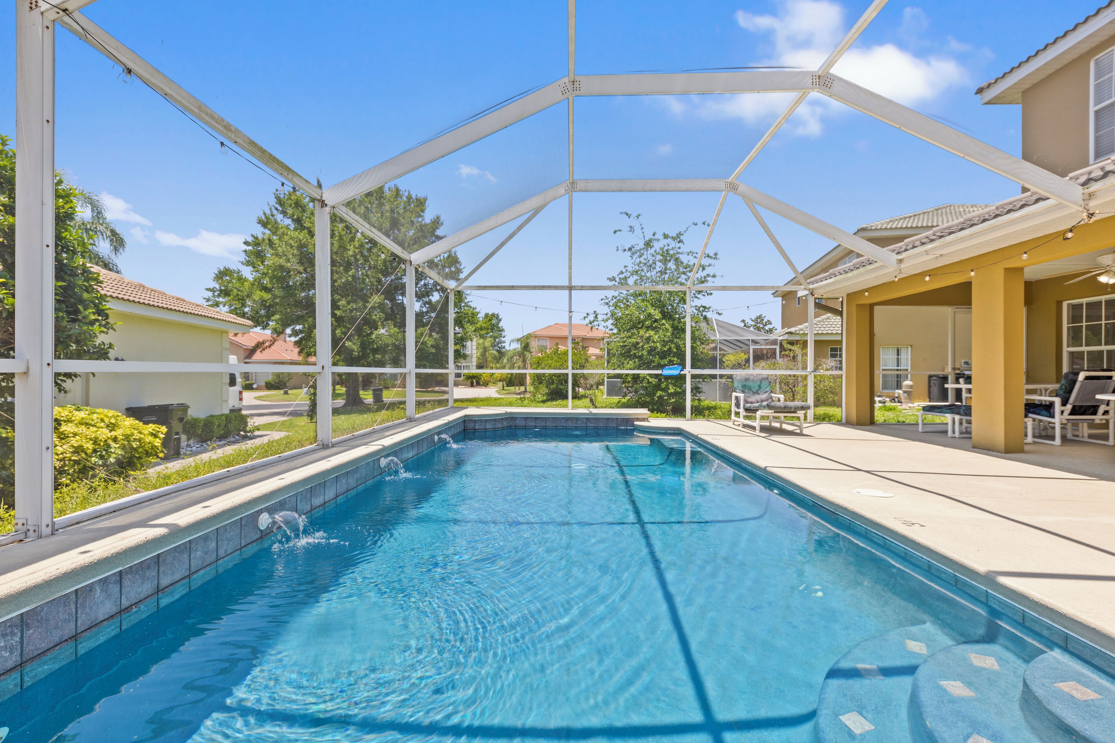 A swimming pool with a covered area, surrounded by a fence, and adjacent to a building with outdoor seating.