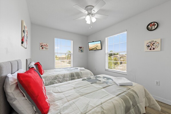 A bedroom with two beds, a ceiling fan, a TV, and artwork on the walls. - 🌟 Spacious 4BR Getaway 🏡 Pool, Privacy & Near Parks 🎢 (Davenport)