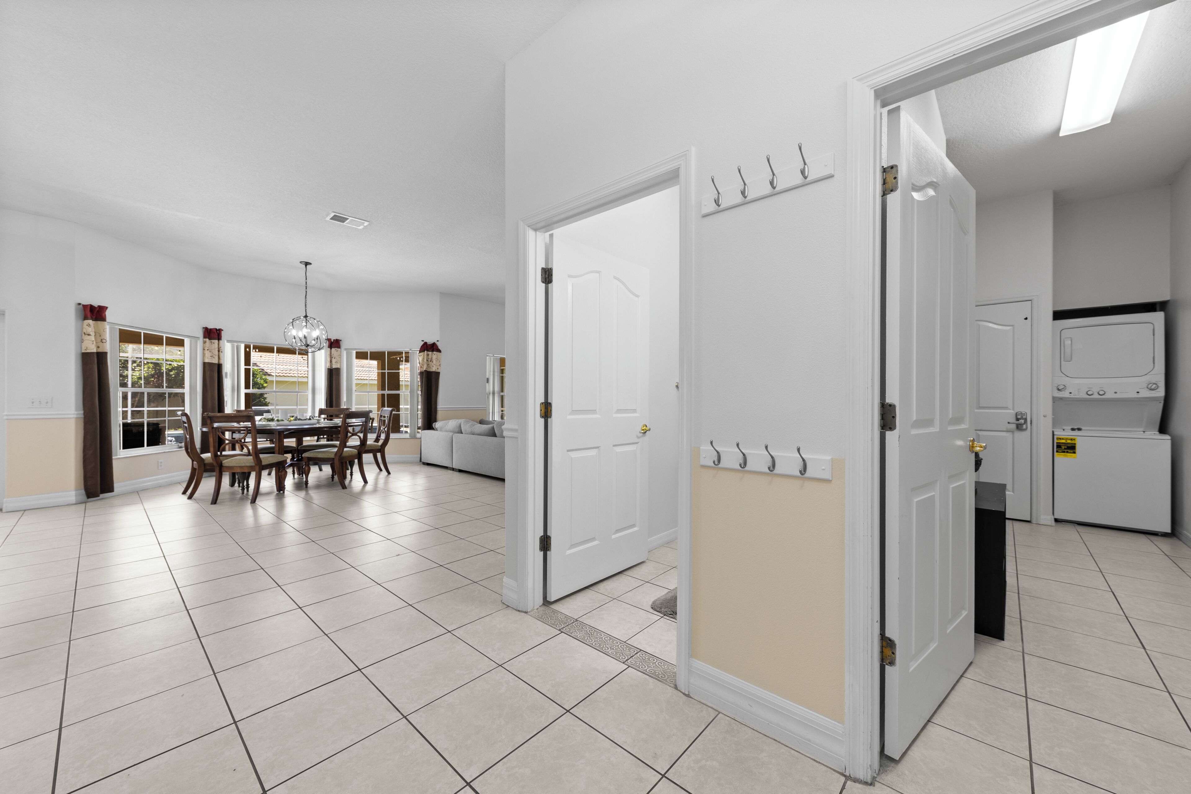 A spacious kitchen with white cabinets, a microwave, and a refrigerator. There is a dining area with a table and chairs, and a window with curtains.