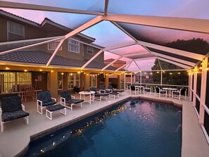 An outdoor swimming pool with lounge chairs and tables, surrounded by a covered patio with string lights. - 🌟 Spacious 4BR Getaway 🏡 Pool, Privacy & Near Parks 🎢 (Davenport)