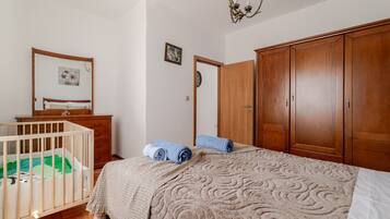 Ein Schlafzimmer mit einem Babybett, einem Holzschrank, einem Bett mit gemustertem Überwurf und einem Wandbild.