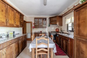 A kitchen with wooden cabinets, a dining table, chairs, a stove, and a sink. - Apartment 'Inferior' with Mountain View, Shared Garden and Wi-Fi (Ponte da Barca)