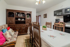 Un'area pranzo con un mobile in legno, un divano con cuscini floreali, un tavolo da pranzo con tovaglia floreale e una televisione sopra il mobile.