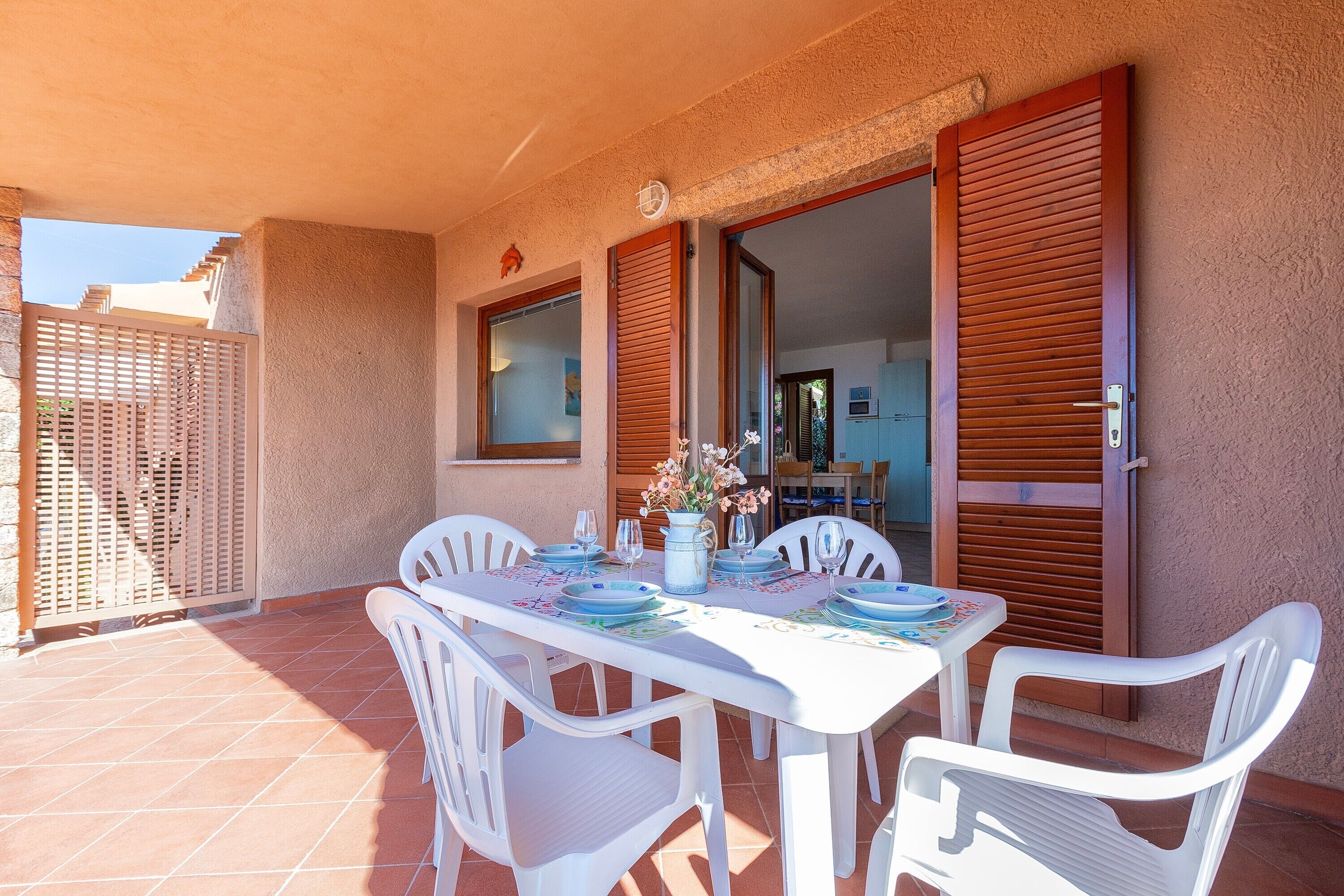 Un patio con una mesa lista para comer, sillas de plástico blanco y una puerta de madera.