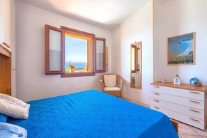 A bedroom with a bed, a dresser, a chair, a window with a view, and a painting on the wall.