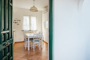 Et spiseområde med et hvidt bord og stole, et vindue med gardiner, og et skilt på væggen der siger "but first Coffee".