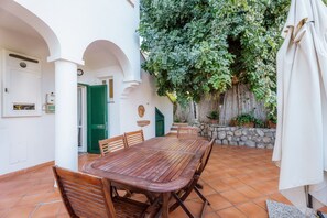 Une terrasse avec une table et des chaises en bois, entourée de murs blancs et de volets verts.