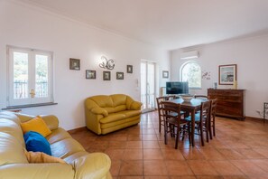 A living room with a yellow sofa, a dining table with chairs, and a TV.