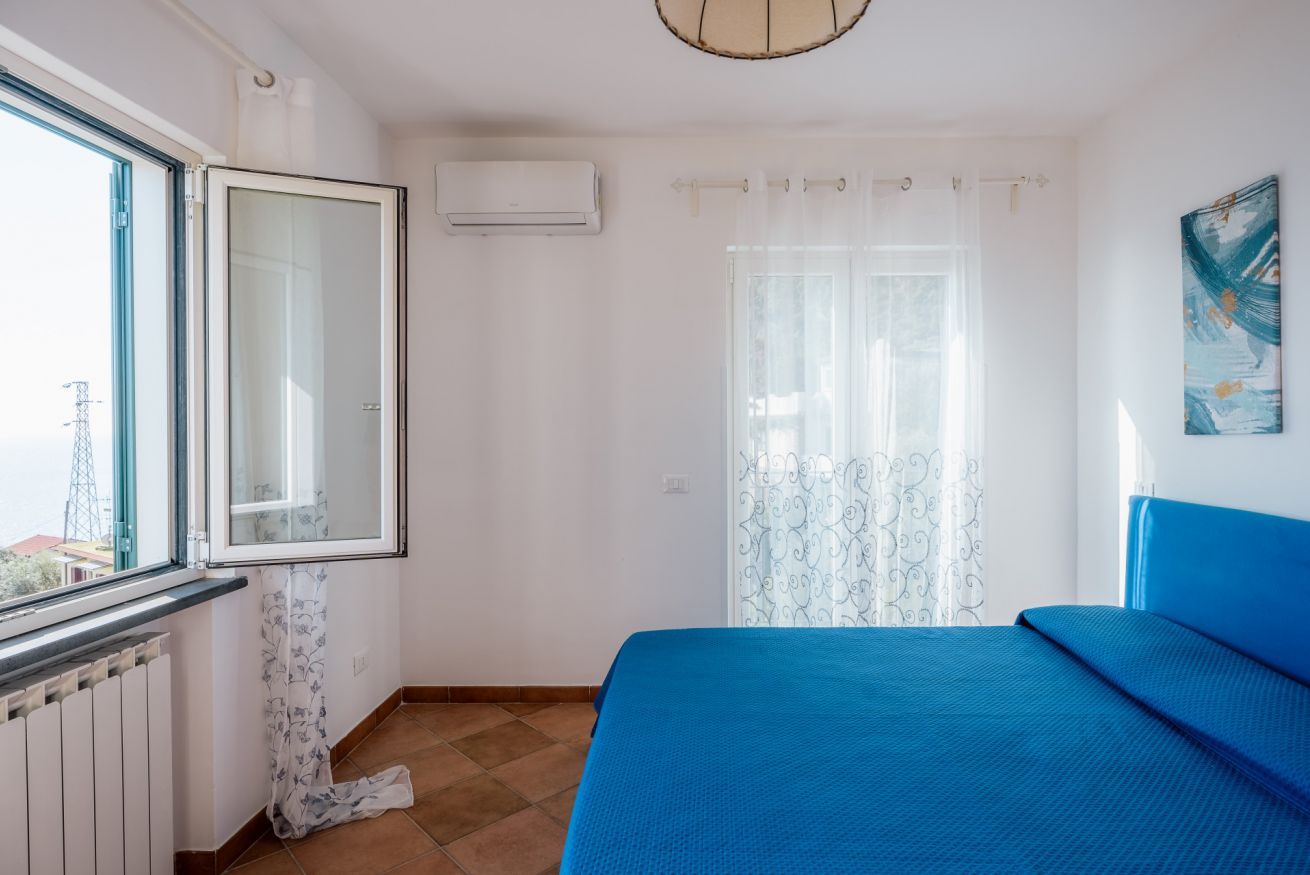 A bedroom with a large window, a radiator, a bed with blue bedding, and a curtain with a floral pattern.