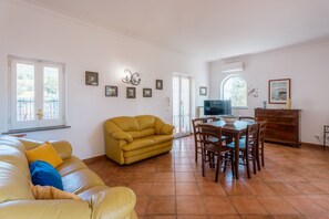 A living room with a yellow sofa, a dining table with chairs, and a TV.