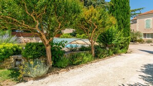 Un jardín con un muro de piedra, un pérgola y un árbol alto.