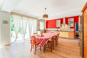 A modern kitchen with wooden cabinets, a red accent wall, and a dining area with a striped tablecloth. - Holiday Home 'Le Secret D'hestia' with Shared Pool, Wi-Fi and Air Conditioning (Bollène)
