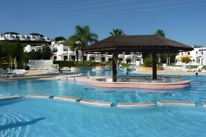 Une piscine avec un jacuzzi central, des chaises longues et un kiosque.
