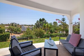 Un balcon avec un canapé, une table et une vue sur un paysage verdoyant, avec des arbres et des bâtiments.