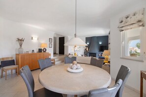 Un coin repas avec une table ronde, des chaises, un luminaire suspendu et une vue sur le salon.