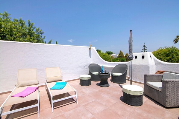 A rooftop terrace with two sun loungers, a small table with chairs, and a wicker sofa.