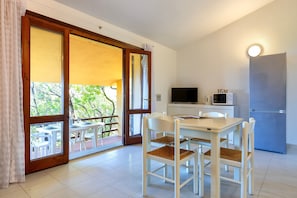 Une pièce comprenant une table à manger, des chaises, un téléviseur, un four à micro-ondes et un réfrigérateur.