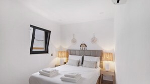 A neatly made bed with white linens and towels, two bedside lamps, a headboard, and a window with a view. - Villa Alvor Rooftop with Sea View, Wi-Fi and Air Conditioning (Alvor)
