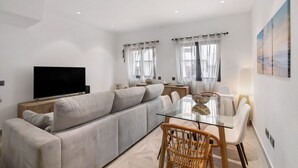 A modern living room with a sofa, a glass dining table, and a TV. - Villa Alvor Rooftop with Sea View, Wi-Fi and Air Conditioning (Alvor)