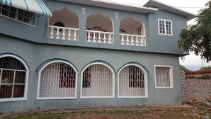 Una casa de dos pisos con un balcón, ventanas arqueadas grandes y un muro de piedra.