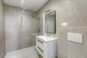 Un baño moderno con cabina de ducha de vidrio, tocador blanco con espejo e interruptor de luz en la pared.