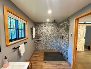 Une salle de bain avec un plancher en bois, une douche avec un mur recouvert de galets, une fenêtre avec un cadre en bois et un porte-serviettes.