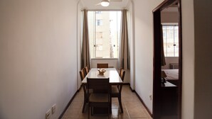 A narrow hallway with a dining area featuring a table and chairs, a ceiling fan, and a view of a building through a window.