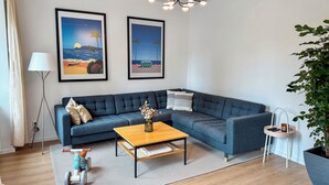 A modern living room with a blue sectional sofa, a wooden coffee table, and two framed landscape paintings.