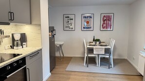A modern kitchen with a built-in oven, a coffee maker, and a dining area with a table set for two. There are three framed pictures on the wall.