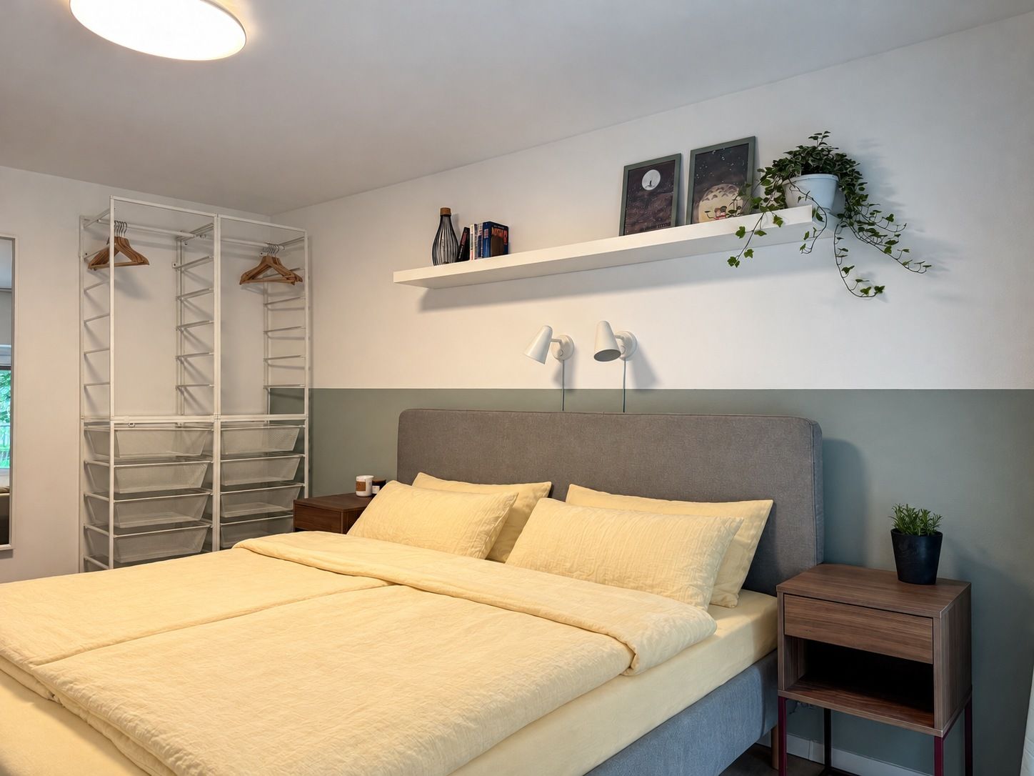 A bedroom with a bed, bedside tables, a wardrobe, and a shelf with decorative items.