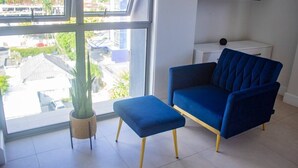 A modern living room with a blue sofa and ottoman, a potted plant, and a TV mounted on the wall.