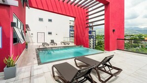 A rooftop pool area with a red and white building, a pool, and lounge chairs.