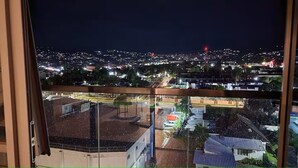 A nighttime cityscape viewed from a balcony with a clear view of the city lights and buildings.