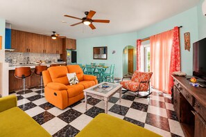 A living room with a checkered floor, orange sofas, a coffee table, and a television on a wooden cabinet.