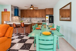 A modern kitchen with wooden cabinets, a central island, and a dining area with a checkered floor.