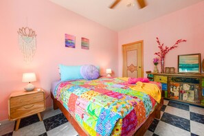 Una camera da letto con una coperta colorata, un comodino in legno, una cassettiera con uno specchio e una porta con decoro a stella.